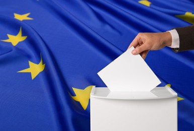 Image of Man putting his vote into ballot box against flag of Europe, closeup. Space for text