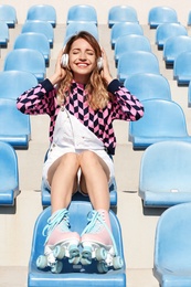 Happy girl with retro roller skates sitting on grandstand