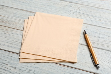 Clean paper napkins and pen on wooden background. Space for text