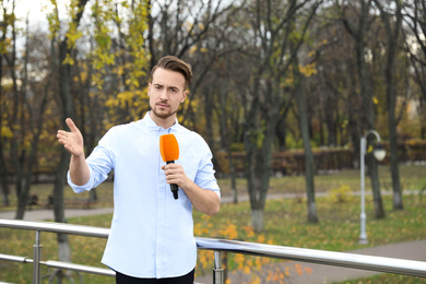 Young male journalist with microphone working in park. Space for text