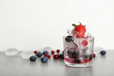 Photo of Glass with frozen berries on gray table