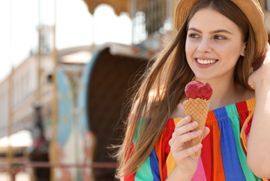 Photo of Young happy woman with ice cream cone in amusement park. Space for text