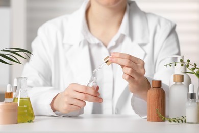 Photo of Dermatologist testing essential oil at white table indoors, selective focus