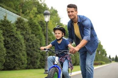 Photo of Dad teaching son to ride bicycle outdoors