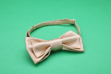 Stylish beige bow tie on green background