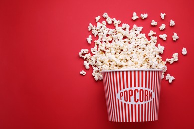 Photo of Overturned paper bucket with delicious popcorn on red background, flat lay. Space for text