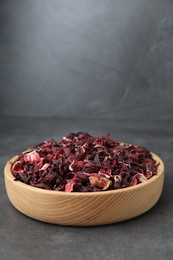 Photo of Hibiscus tea. Wooden bowl with dried roselle calyces on grey table. Space for text