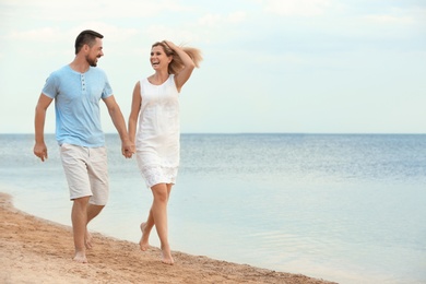 Happy romantic couple running together on beach, space for text