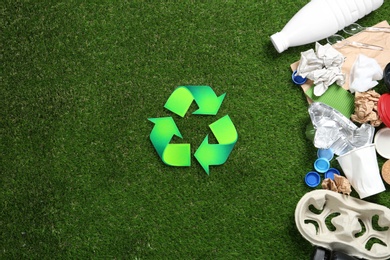 Photo of Flat lay composition with recycling symbol, different garbage and space for text on green grass