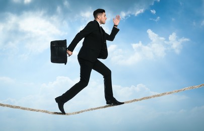 Image of Risks and challenges of entrepreneurship. Businessman with portfolio running on rope in cloudy sky