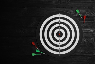 Photo of Dart board with color arrows on black wooden background, top view. Space for text