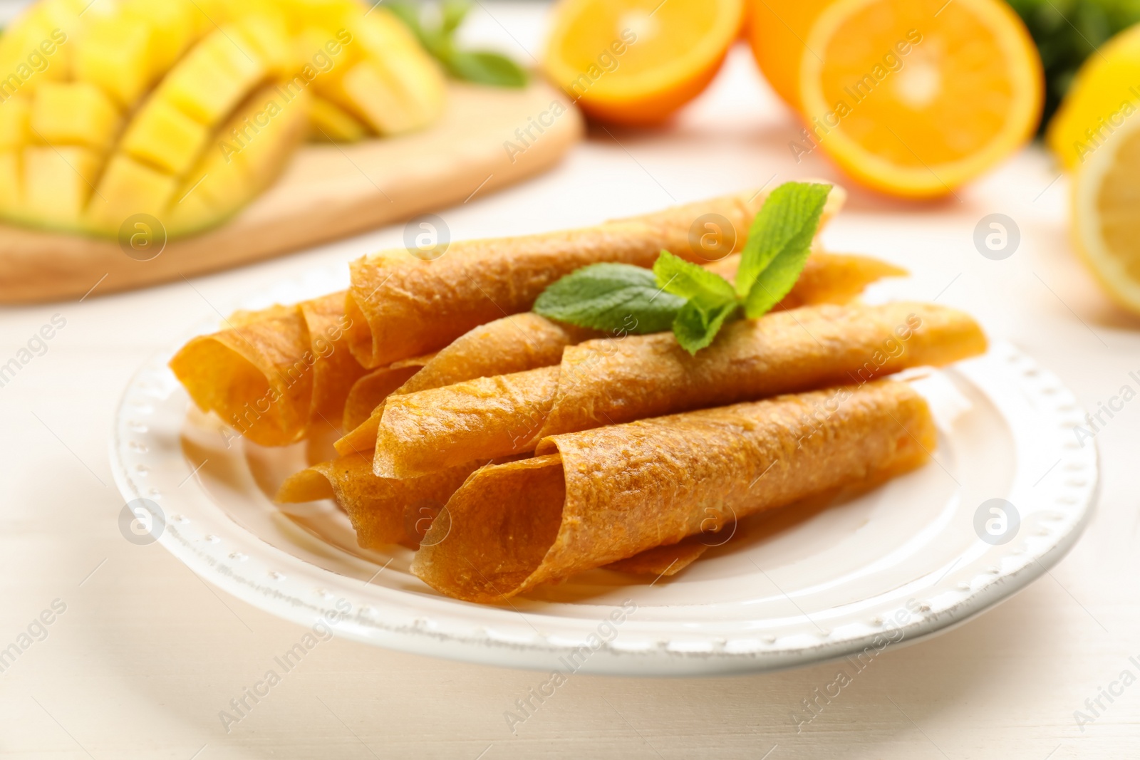 Photo of Composition with delicious fruit leather rolls and mint on white wooden table, closeup