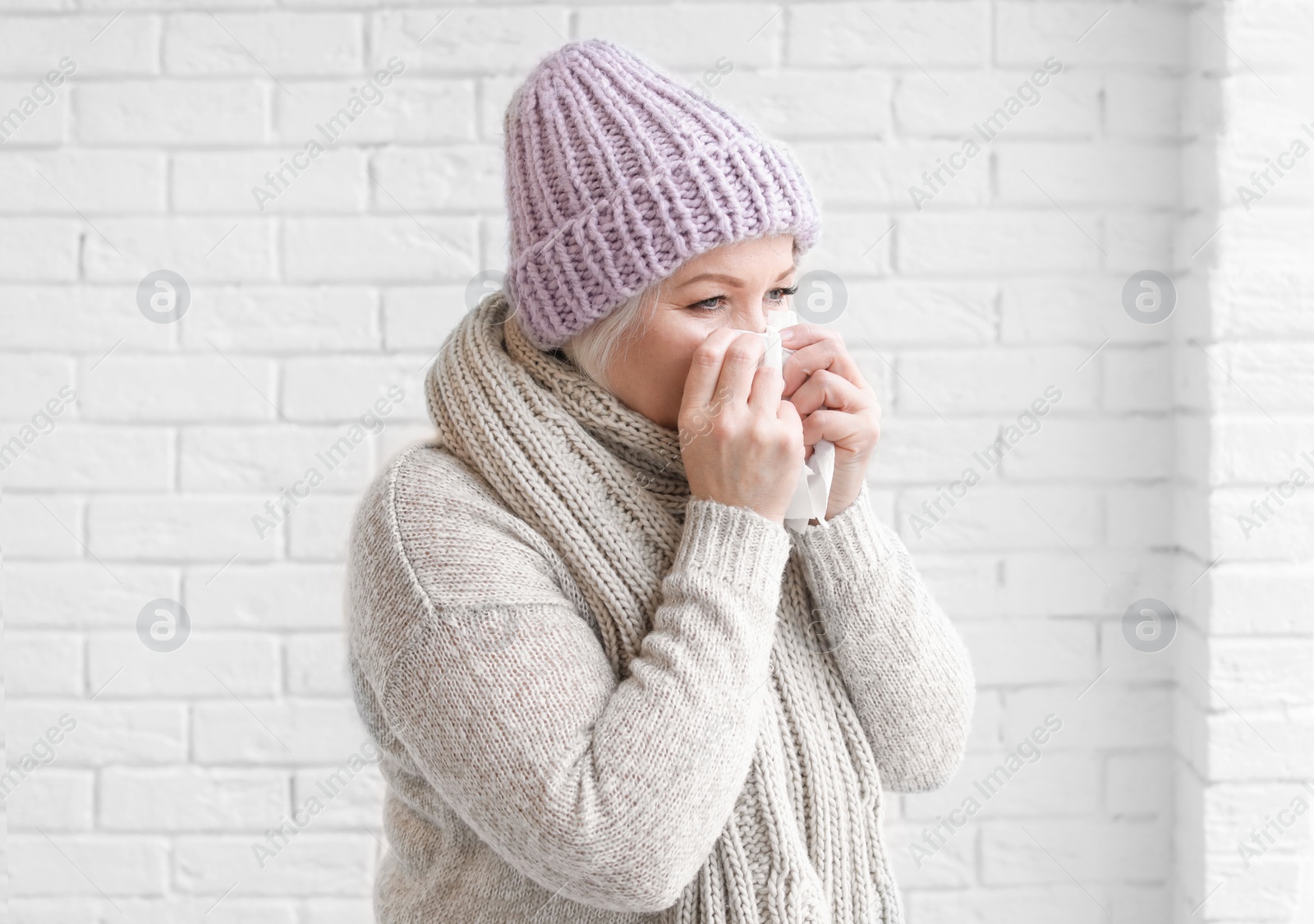 Photo of Mature woman in warm clothes suffering from cold on brick background