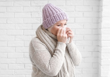 Mature woman in warm clothes suffering from cold on brick background