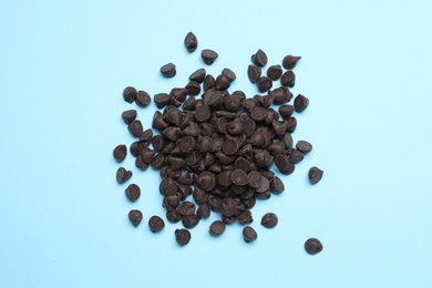 Photo of Pile of delicious chocolate chips on light blue background, top view