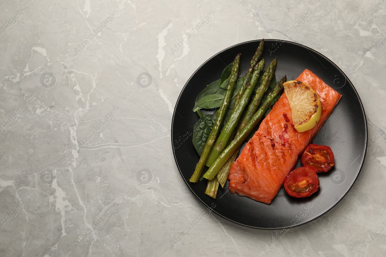 Photo of Tasty grilled salmon with tomatoes, lemon and asparagus on grey table, top view. Space for text