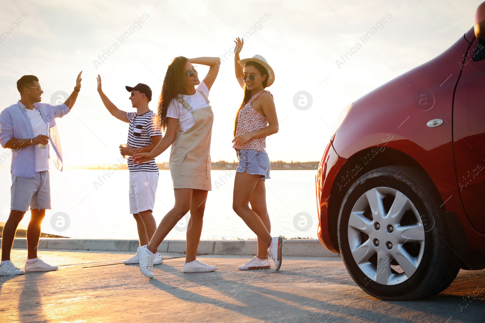 Photo of Happy friends having fun near car outdoors at sunset. Summer trip