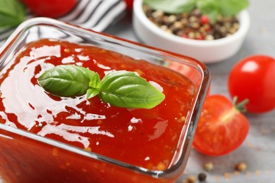 Photo of Spicy chili sauce with basil on grey table, closeup