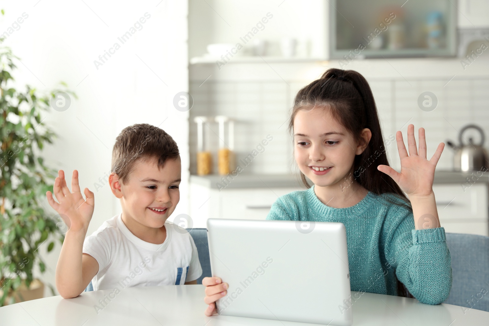 Photo of Little children using video chat on tablet at table in kitchen