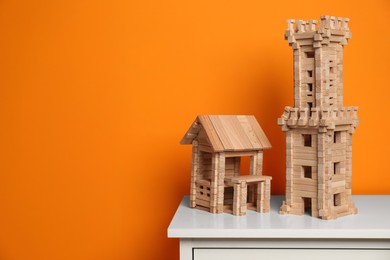 Photo of Wooden tower and house on white chest of drawers near orange wall, space for text. Children's toys