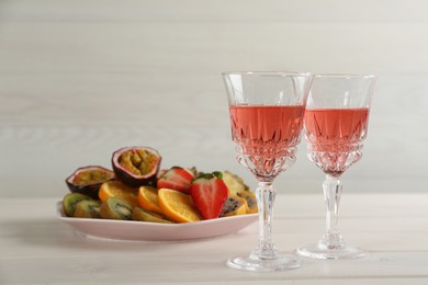 Delicious exotic fruits and glasses of wine on white wooden table