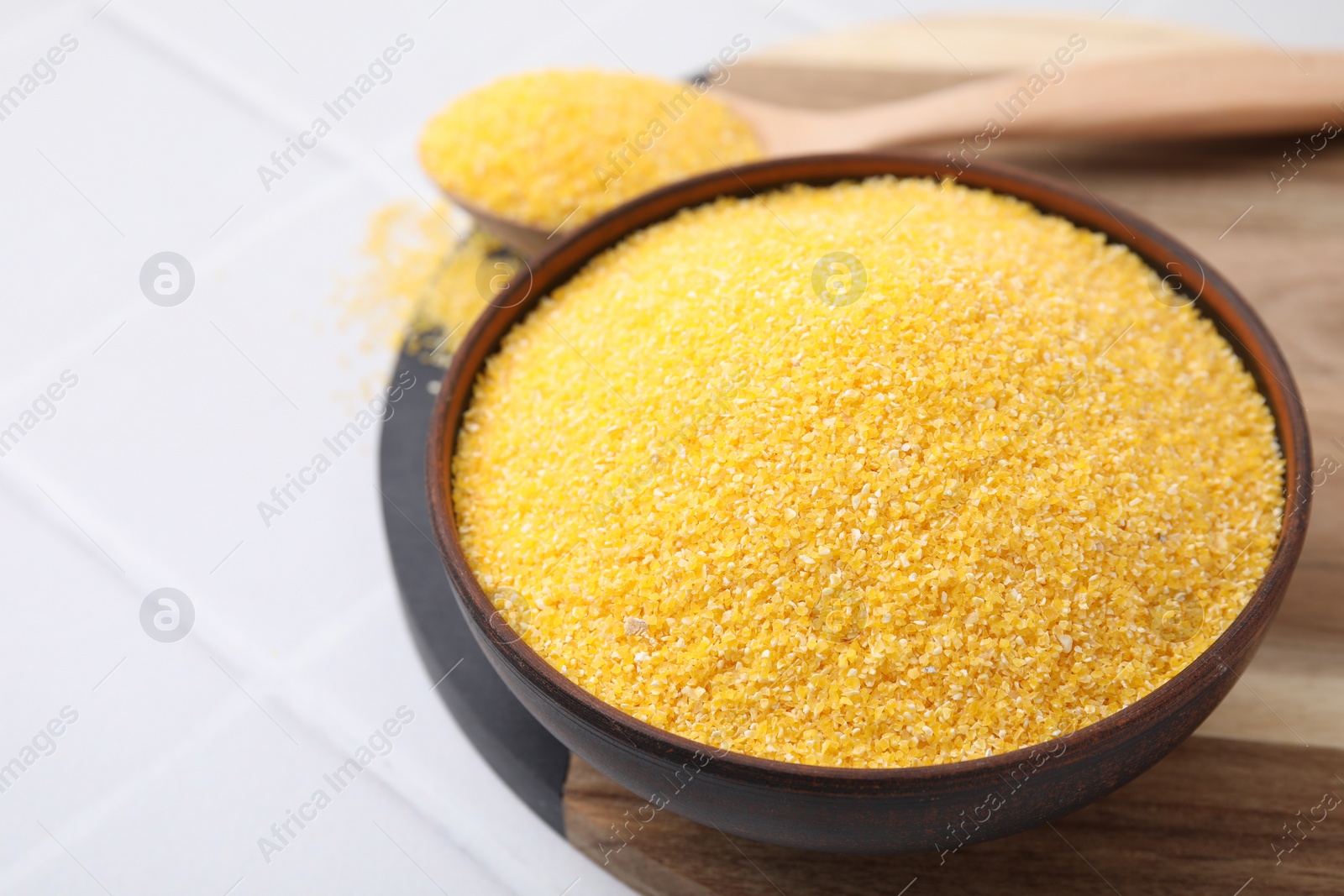 Photo of Raw cornmeal in bowl on white tiled table, closeup. Space for text