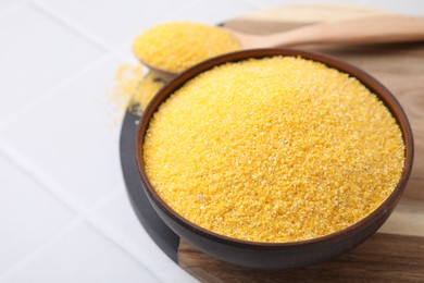 Raw cornmeal in bowl on white tiled table, closeup. Space for text