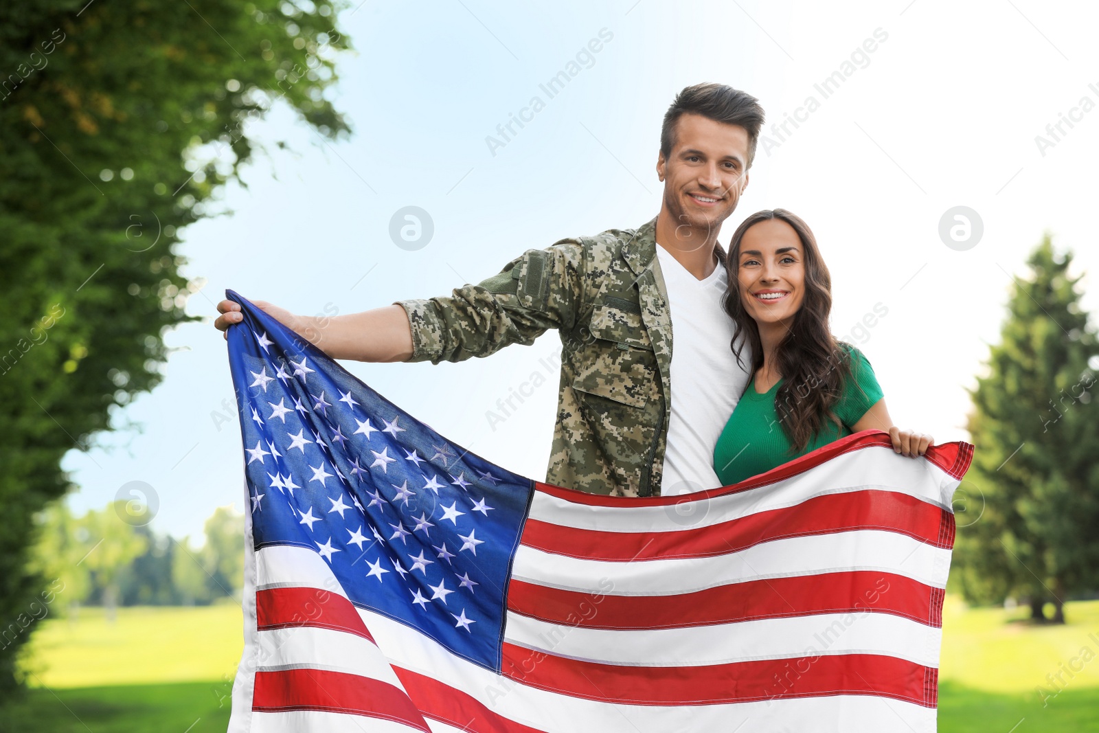 Photo of Man in military uniform with American flag and his wife at sunny park