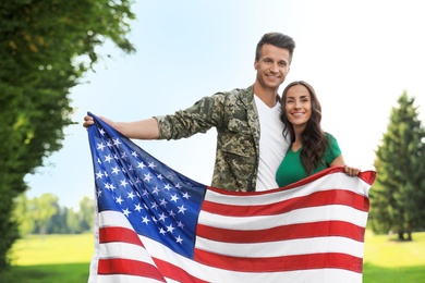 Man in military uniform with American flag and his wife at sunny park