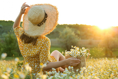 Photo of Woman with straw hat and handbag full of chamomiles resting in meadow