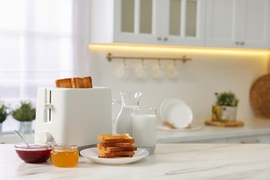 Photo of Making toasts for breakfast. Appliance, crunchy bread, honey, jam and milk on white marble table in kitchen. Space for text