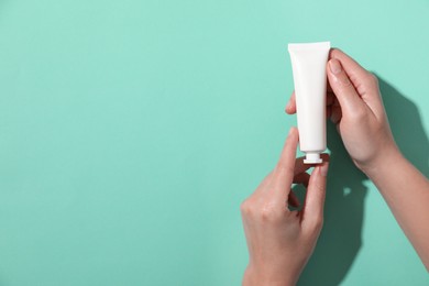 Woman with tube of hand cream on turquoise background, top view. Space for text