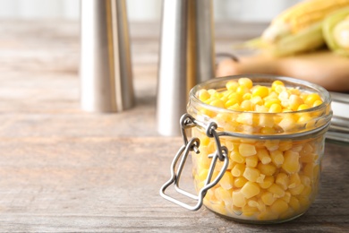 Jar with corn kernels on wooden table. Space for text