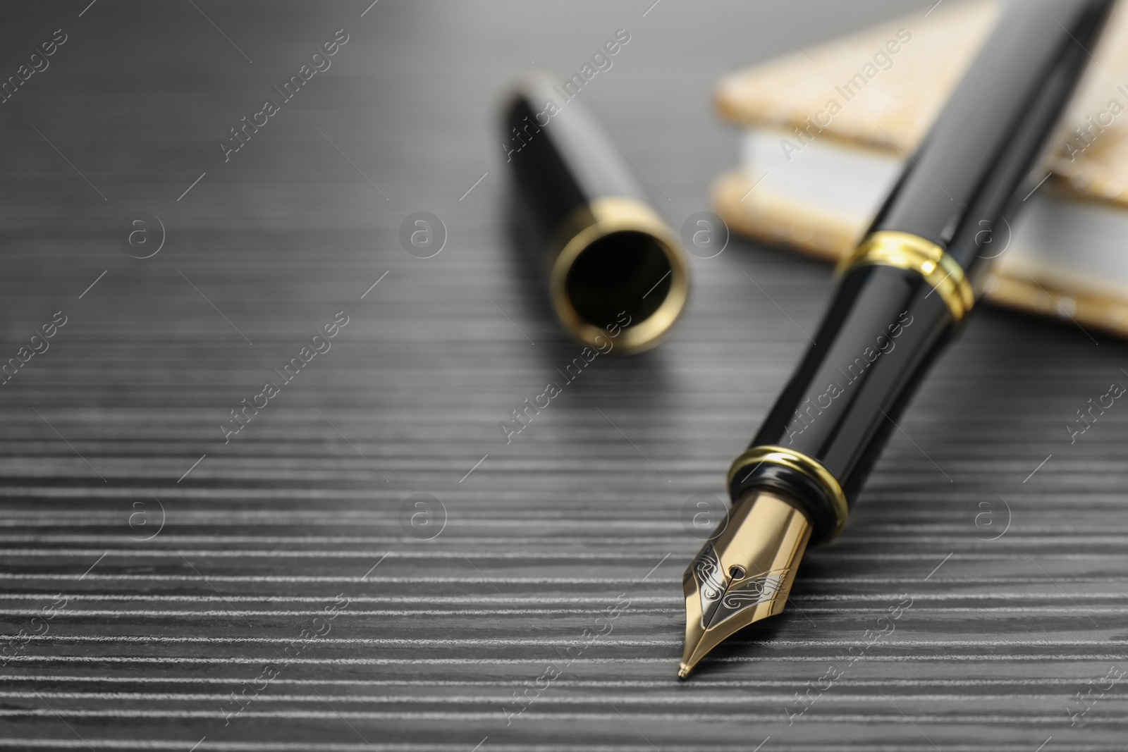 Photo of Stylish fountain pen and notebook on black wooden table, closeup. Space for text