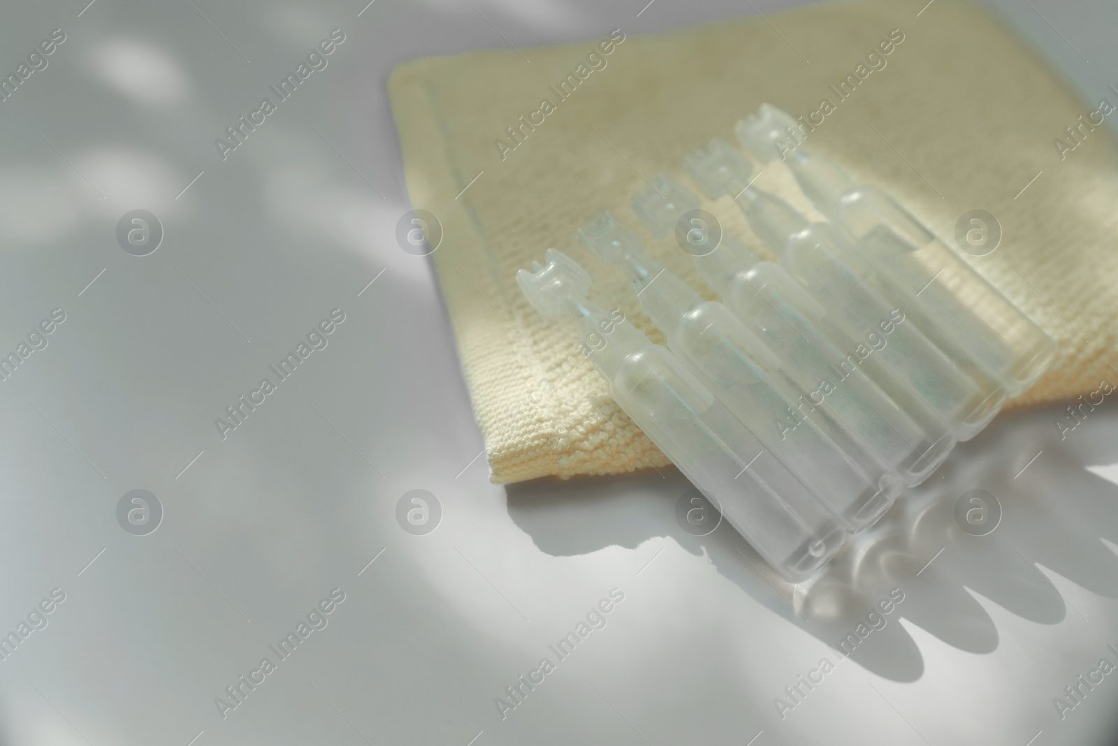 Photo of Single dose ampoules of sterile isotonic sea water solution and towel on white table, closeup. Space for text