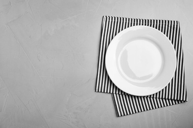 Photo of Empty ceramic plate and towel on light grey table, flat lay. Space for text