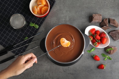 Photo of Woman dipping tangerine into pot with chocolate fondue on gray background, flat lay