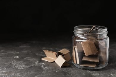 Photo of Glass jar with paper pieces on grey table, space for text