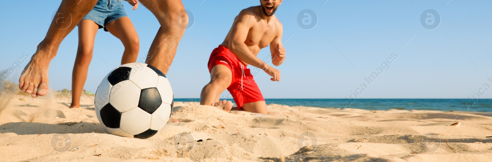 Image of Group of friends playing football on sandy beach, low angle view. Banner design with space for text