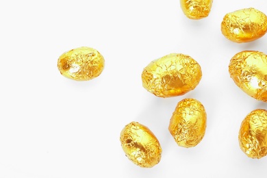 Many chocolate eggs wrapped in bright golden foil on white background, top view