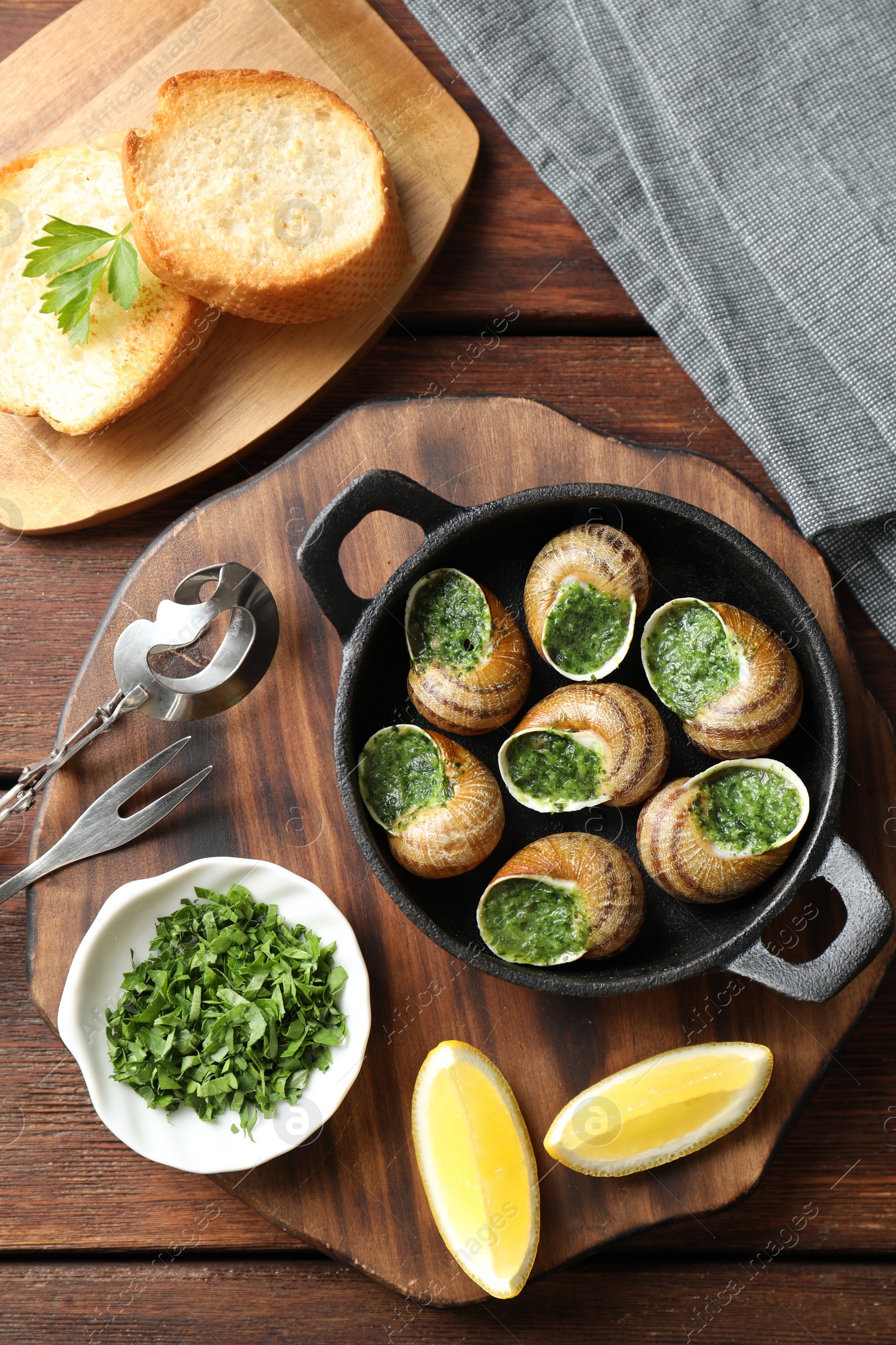 Photo of Delicious cooked snails in baking dish served on wooden table, flat lay