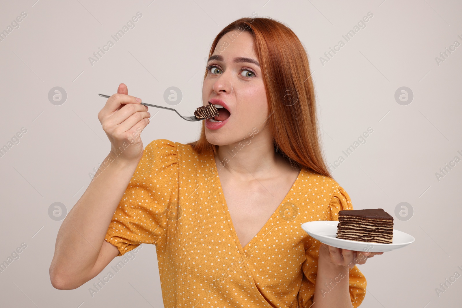 Photo of Young woman eating piece of tasty cake on light grey background