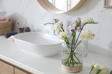 Photo of Beautiful freesia flowers on countertop in bathroom