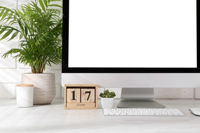 Photo of Office workplace with computer, wooden block calendar and houseplants on light table near white brick wall