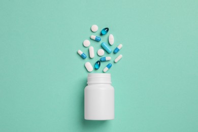 Photo of Plastic medical bottle with many different pills on turquoise background, flat lay