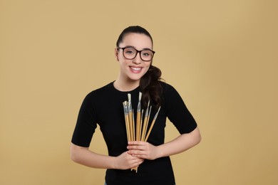 Photo of Woman with paintbrushes on beige background. Young artist