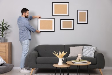 Photo of Man hanging picture frame on gray wall at home