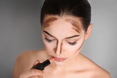 Photo of Young woman applying lipstick on grey background. Professional makeup products