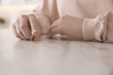 Image of Woman holding wedding ring at table indoors, closeup. Cheating and breakup