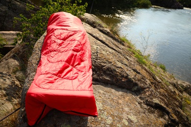 Photo of Man resting in sleeping bag on cliff near lake